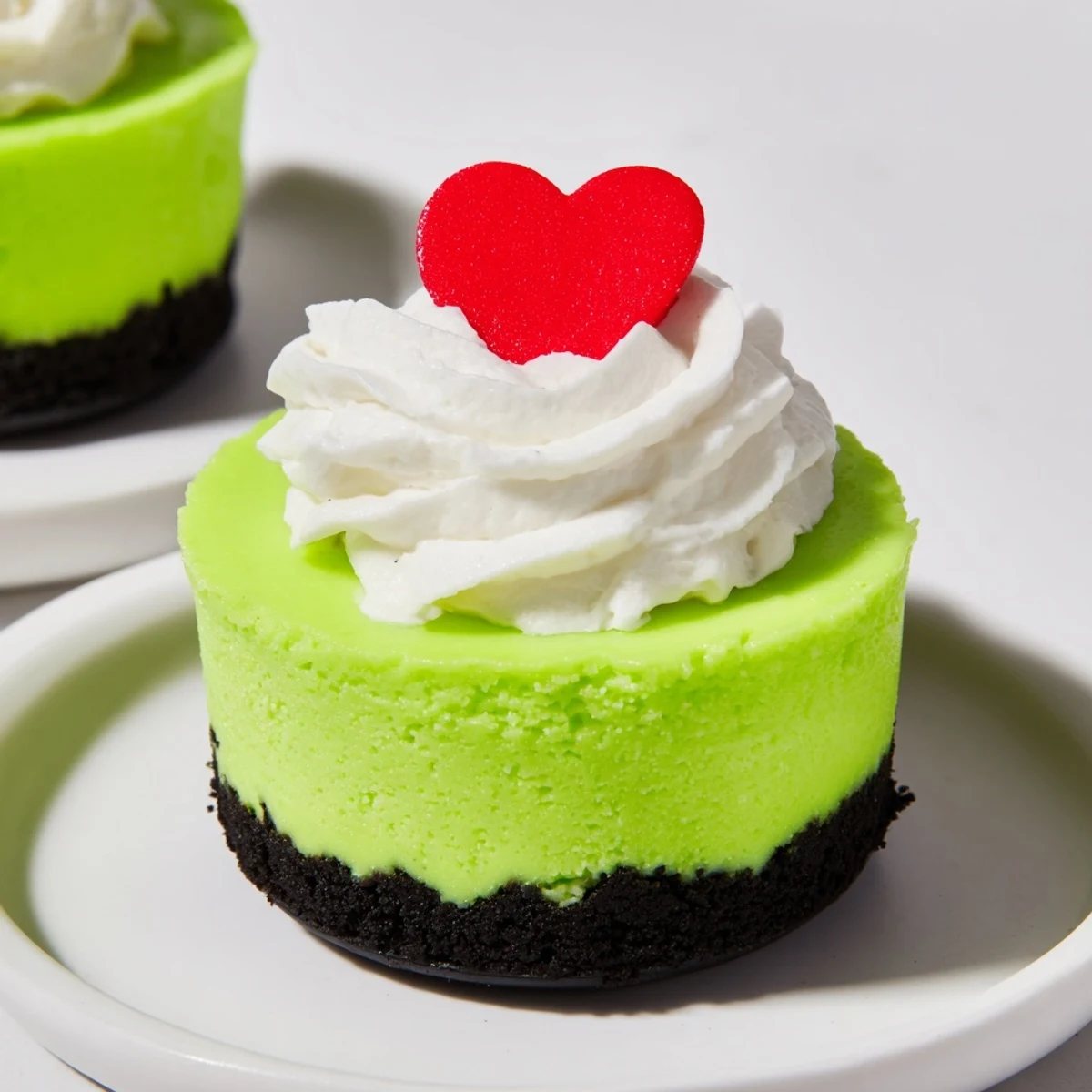 Festive Grinch Mini Cheesecakes topped with whipped cream and red heart sprinkles, a perfect holiday dessert.