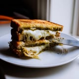 A crispy Sourdough Pesto Grilled Cheese sandwich served beside a warm bowl of tomato soup.