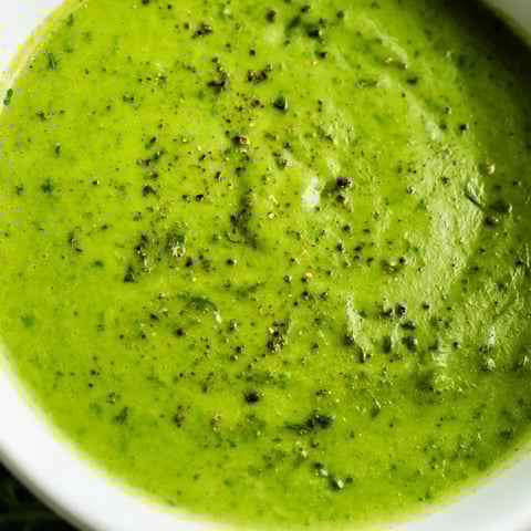 A close-up of Big Green Immunity-Boosting Vegetable Soup in a rustic bowl, topped with fresh spinach leaves and a lemon wedge.