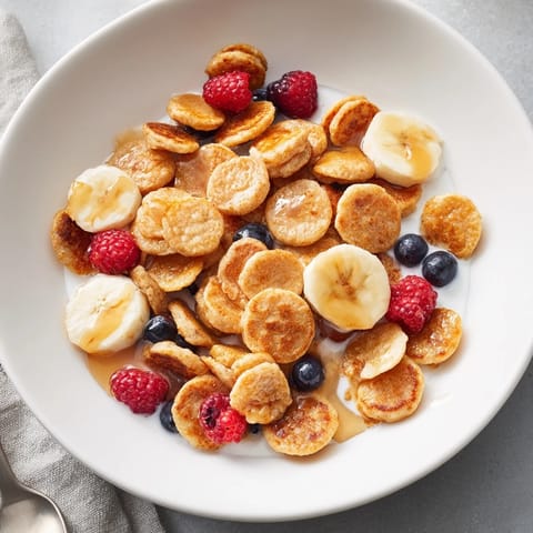 Bite-sized pancake cereal in a bowl, drizzled with maple syrup and milk.  