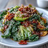Spicy cabbage stir fry in a hot wok with sizzling garlic, ginger, and chili, garnished with sesame seeds.